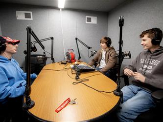 four students in a video production class sitting at a table with microphones